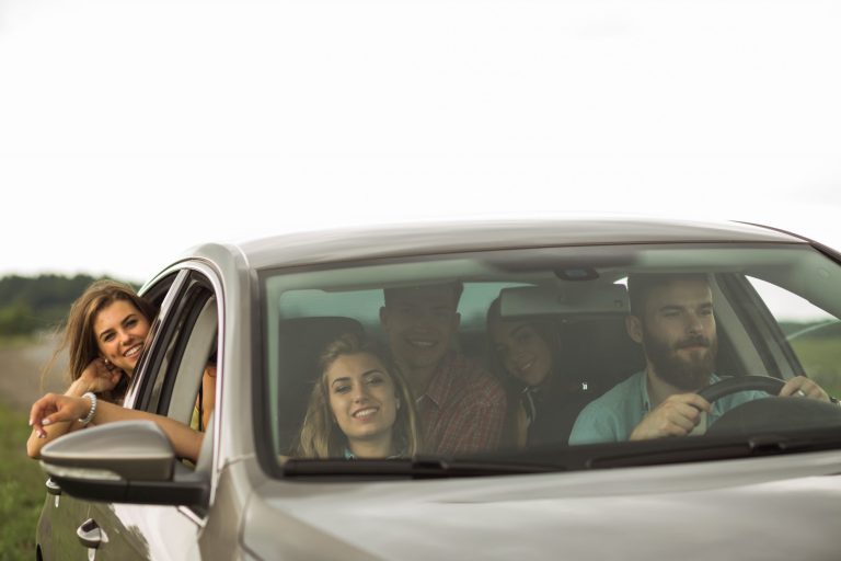 Group of people in car with side-view mirror in the foreground.